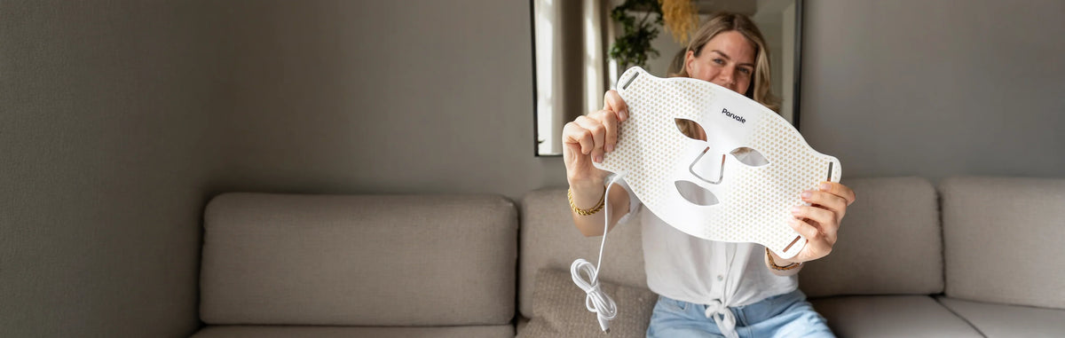 Woman holding a white LED face mask for skincare treatment in a living room.
