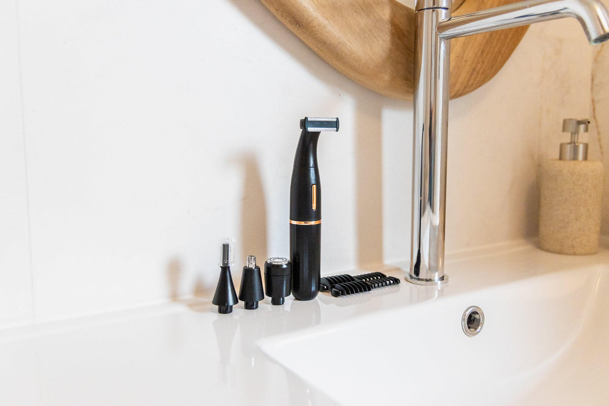 Black electric facial cleansing brush and exfoliating attachments on a white bathroom sink.